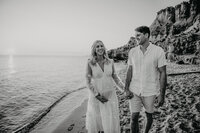 husband and wife stroll on the beach at maternity session in black and white