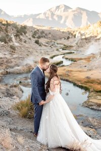 A bride and groom kiss in front of steamy hot creek geological site near Mammoth Lakes. 