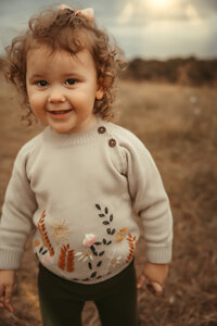 Little girl wearing an embroidered crewneck sweater, black pants and a bow