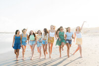 Nicole Marie Photography's senior model team running down the beach in Ocean CIty, New Jersey. They are wearing yellow, green and blue summer outfits.