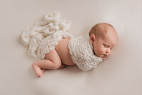 Newborn baby girl photographed by Atlanta, Georgia newborn photographer baby is  laying on side, asleep, with white lace fabric wrapped around her arms and bottom on white fabric backdrop