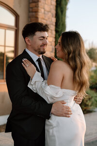 A man and woman holding each other while they look into each others eyes and smile at each other at Monte de Oro Winery in Temecula, California. 