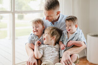 A dad holds twin babies and a toddler on his lap and they are all laughing, captured by San Antonio lifestyle photographer Cassey Golden.