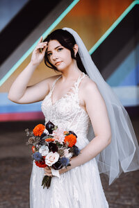 A bride poses with her beautiful bouquet in front of a colorful striped wall