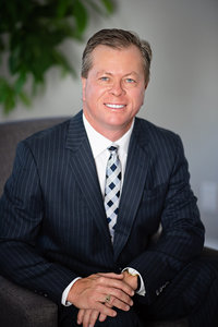 Headshot of Financial Advisor from Rae Lipskie wearing a business suit and tie, sitting in grey chair in front of plant in photography studio KW Headshots.