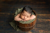 Newborn girl posed in a bucket during her baby picture session at Jennifer Brandes Photography.