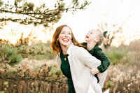 Mother in green dress giving a piggy back ride to her laughing daughter at Eldridge Park in Elmhurst