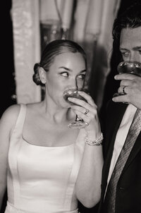 Black and white film photo of a newlywed couple sipping cocktails during their wedding reception — a candid moment captured by a film wedding photographer.