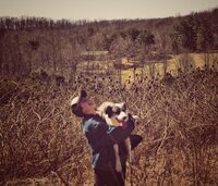 Women in black cowboy hat poses with two dogs on a farm overlooking the hills.