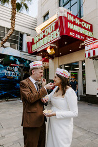 A newlywed couple sharing fries outside of an In-N-Out with paper hats on 