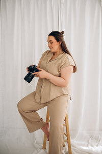 A person sitting on a stool looking down at a camera