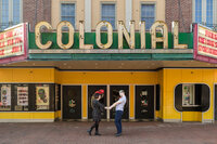 Engaged couple sharing a moment in front of the vibrant marquee of the Colonial Theater in Phoenixville.