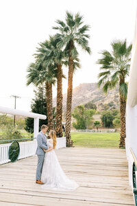 bride and groom standing on bridge with palm tree and sunset in background