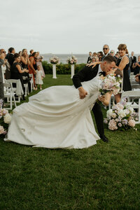 Couple shares their first kiss as bride and groom at the end of the aisle after their Ceremony at Misselwood in Beverly, MA as the groom dips the bride