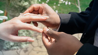 grrom puts on wedding band on bride's hands, outdoor at the round lake vineyards wedding venue