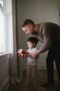 dad helps his son learn how to play with a wooden airplane