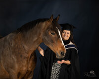 A graduation photo of a horse and a girl with graduation robe and hat