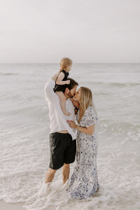 A family on the beach - child is sitting on dad's shoulders, mom and dad are kissing