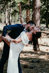 Groom dipping bride for a kiss in a pine forest during their Lake Tahoe elopement.