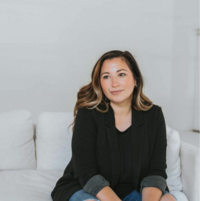 Creative woman casually sitting on a couch, looking off-camera with a warm, thoughtful expression.