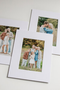 Four printed photographs with white mat lay on table together, showing printed photos of a young family with two children
