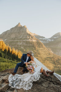 Bride and groom sitting on a rock in front of a mountain range during their Glacier National Park elopement.
