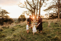 Michaela and her husband and two children holding hands for a pose during their sunset photoshoot with family photographer michelle kelly