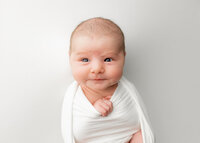 newborn baby girl wrapped in a white jersey swaddle with her eyes open