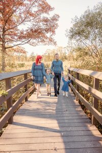 Family of four walking across bridge, holding hands at sunset.