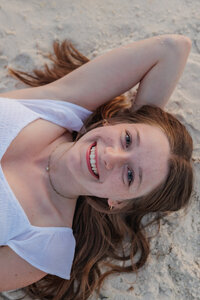 High school senior laying on the beach in a close up. Her right hand is behind her head.