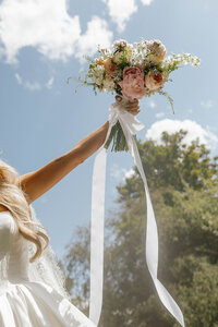 Bride holding her wedding bouquet high in the air with flowing white ribbons, captured by a Washington wedding photographer.