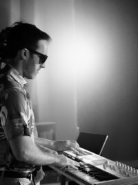 Close-up of synth player focused on keys under red and violet lighting – cinematic behind-the-scenes brand image by Mewphotovideo