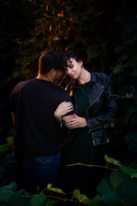 Couple holding arms and snuggling surrounded by green vines.