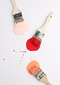 Paint brushes with light pink, coral, and red paint on white background