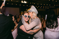 Emotional reception hug between Texas wedding photographer, Erin Marcin and bride in sequin dress, captured in a candid, high-end documentary style with flash.

