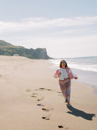 A person wearing pink and white runs along a beach.