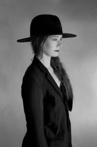 black and white photo of a woman standing sideways in a black hat