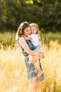 A mother and daughter hug in a field on a sunny day