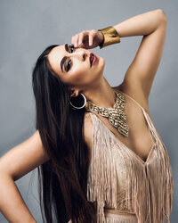Fashion portrait inspired by singer Cher with a woman wearing a fringe jumpsuit jeweled necklace and gold bracelet