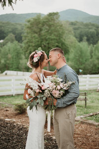 Couple kissing in the mountain on their wedding day with flower bouquet
