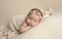 newborn baby girl sleeping on belly and wrapped with a soft buttery cream blanket and wearing a cream-flowered headband.