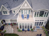Aerial view of the back of a large house with a composite deck on top of a sun room in the center. 