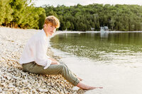 teen guy sitting on a beach in door county at sunset for his senior portraits