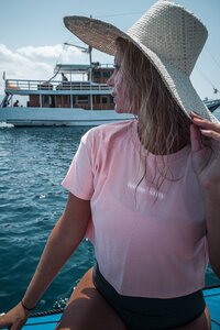 Blonde tanned girl with back to camera looking out at the ocean wearing black jumpsuit and holding hair up