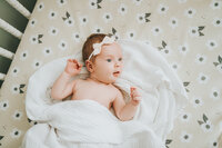 Newborn baby girl with eyes open looks off camera while laying in  crib during newborn photography session
