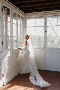 photo of bride standing in front of large windows wearing her wedding gown and veil taken by Wisconsin elopement photographer