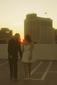 An engaged couple holds one another's faces close and giggle during an intimate moment in the sunset