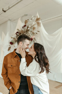 Photo of a couple - female, Aislynn Palmer Wedding photographer, with long brown hair - holding the man's face smiling and looking at eachother.