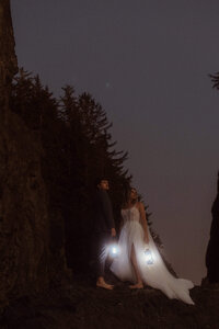 A wedding couple standing on a rock with lanterns on Oregons coast