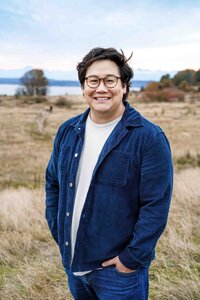 Seattle man stands for headshot outside at Discovery Park near waterfront during family portrait session wearing corduroy jacket and jeans